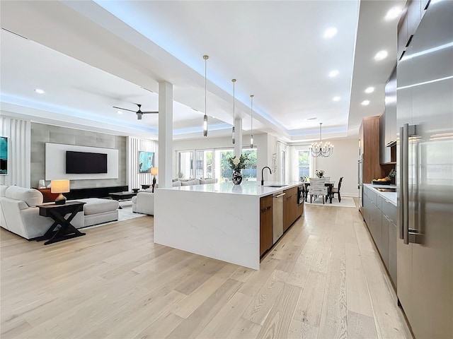 kitchen with light stone counters, light hardwood / wood-style flooring, hanging light fixtures, appliances with stainless steel finishes, and a large island with sink