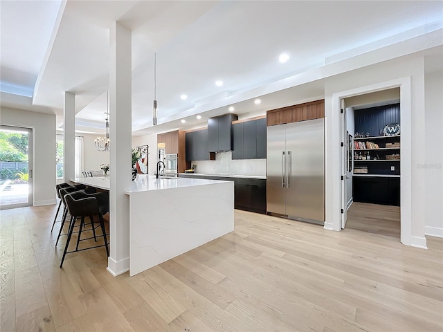 kitchen featuring light stone countertops, a kitchen bar, light wood-type flooring, built in refrigerator, and pendant lighting