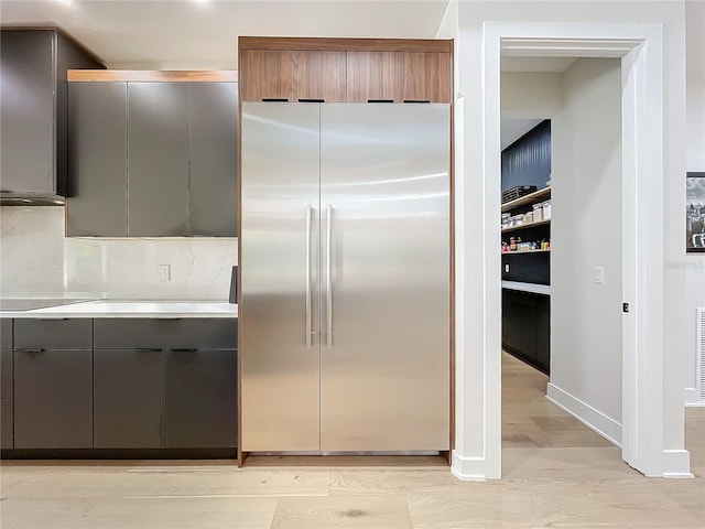 kitchen featuring stainless steel built in refrigerator, decorative backsplash, and light hardwood / wood-style flooring