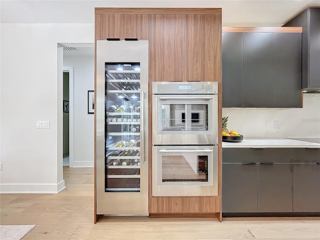 kitchen featuring black electric cooktop, backsplash, double oven, light wood-type flooring, and wine cooler