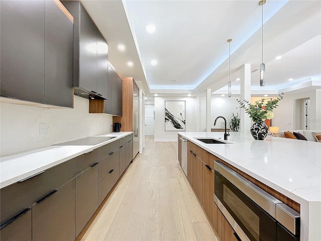 kitchen with light stone counters, hanging light fixtures, sink, a raised ceiling, and light wood-type flooring