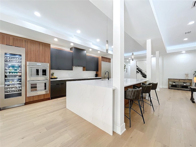 kitchen with appliances with stainless steel finishes, wine cooler, light wood-type flooring, and decorative light fixtures