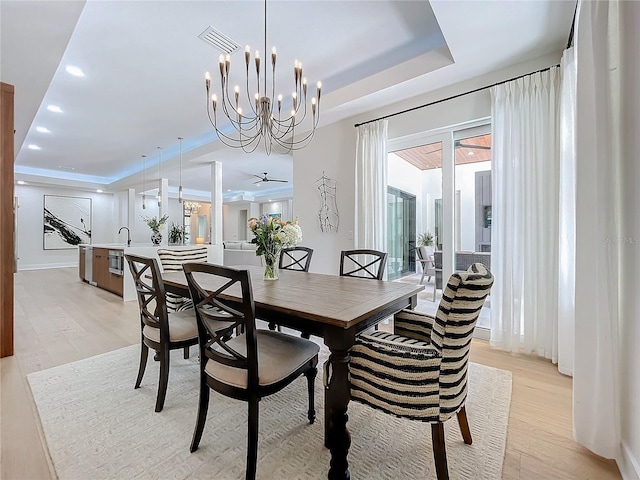 dining area featuring sink, light wood-type flooring, ceiling fan with notable chandelier, and a raised ceiling