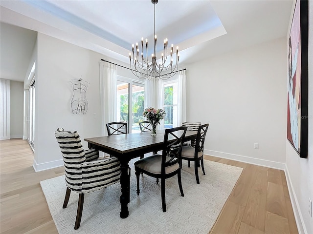 dining space featuring a chandelier, light wood-type flooring, and a tray ceiling