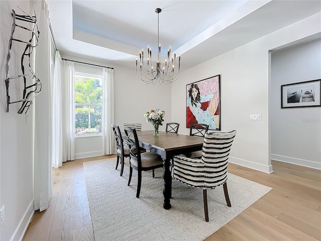 dining space with a raised ceiling, light hardwood / wood-style flooring, and a notable chandelier