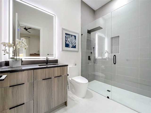 bathroom with toilet, vanity, a shower with door, and ceiling fan