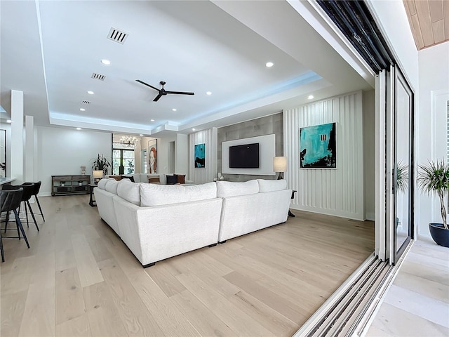 living room with ceiling fan with notable chandelier, light hardwood / wood-style floors, and a raised ceiling