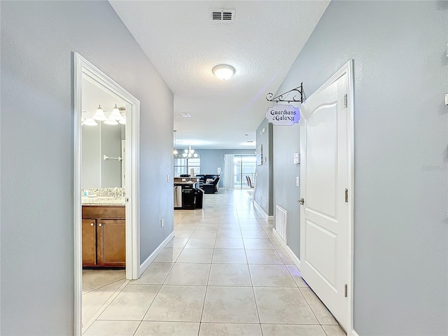 hall featuring a chandelier, a textured ceiling, and light tile patterned floors