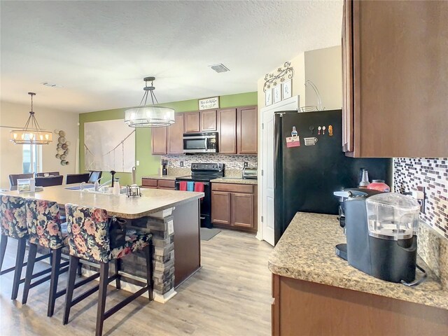 1927 Partin Terrace Rd, Kissimmee, FL 34744 - kitchen with black range with electric stovetop, stainless steel microwave, a sink, decorative backsplash, and a breakfast bar
