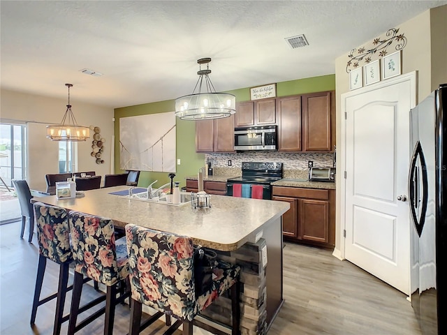 kitchen with decorative light fixtures, a kitchen island with sink, a kitchen breakfast bar, and stainless steel appliances