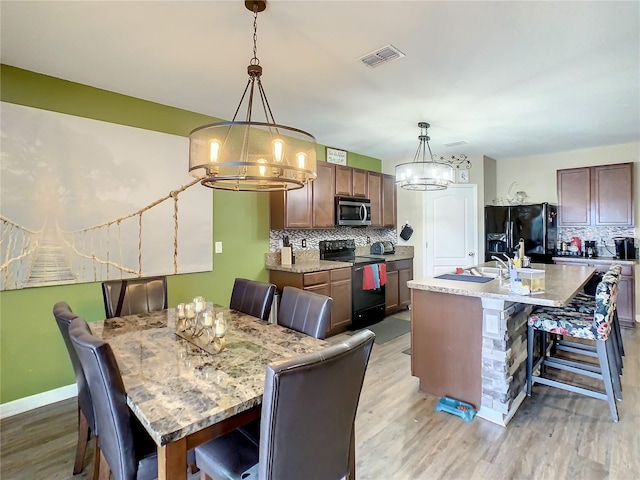 dining room with light wood-type flooring, a notable chandelier, and sink