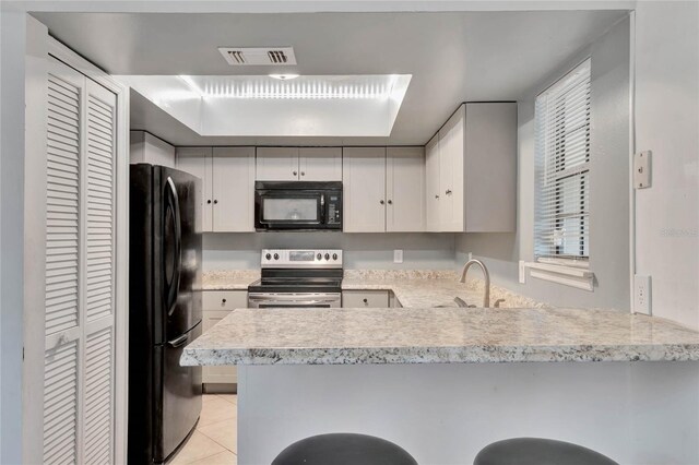 kitchen featuring kitchen peninsula, sink, black appliances, light tile patterned floors, and white cabinetry