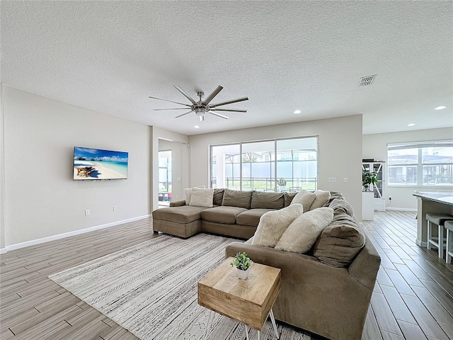 living room with plenty of natural light, light hardwood / wood-style floors, a textured ceiling, and ceiling fan