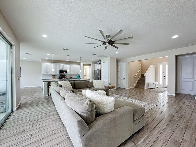 living room featuring ceiling fan, light hardwood / wood-style floors, and a textured ceiling