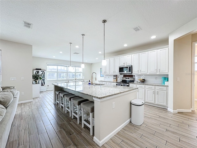 kitchen featuring appliances with stainless steel finishes, white cabinetry, and a kitchen island with sink