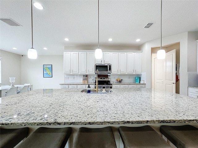 kitchen featuring sink, hanging light fixtures, a spacious island, decorative backsplash, and appliances with stainless steel finishes