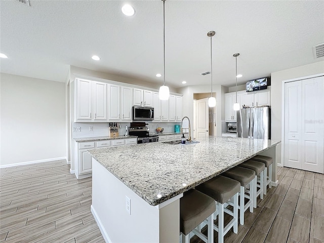 kitchen featuring white cabinets, a large island with sink, stainless steel appliances, and sink