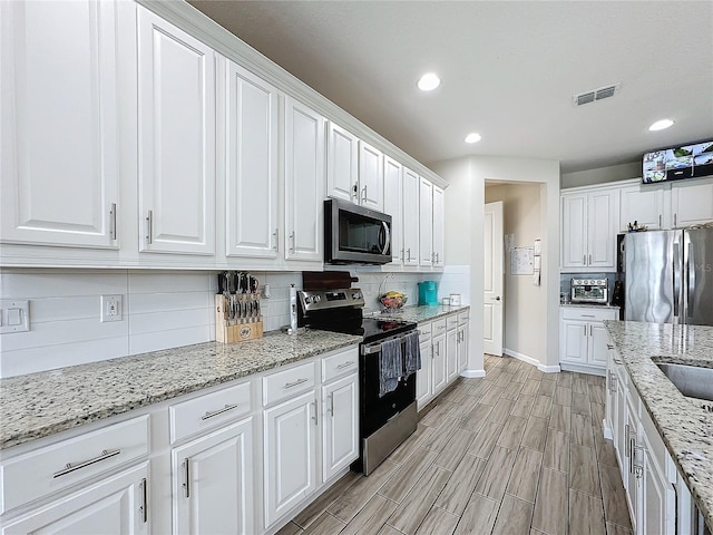 kitchen with white cabinets, decorative backsplash, light wood-type flooring, light stone countertops, and stainless steel appliances