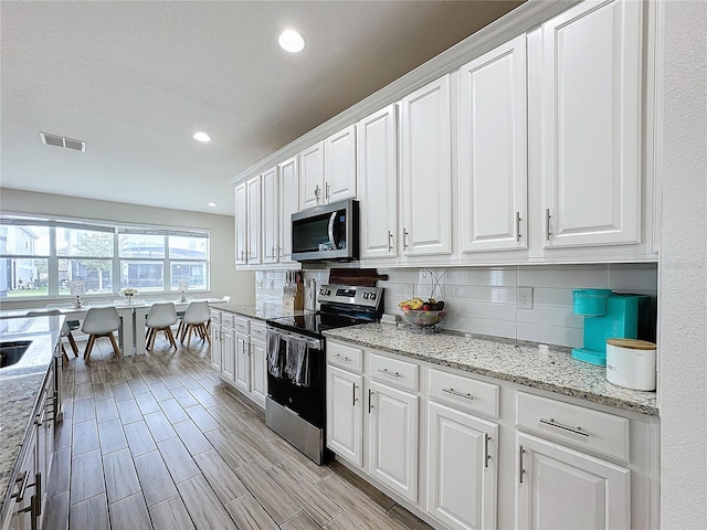 kitchen featuring decorative backsplash, light stone countertops, light hardwood / wood-style floors, white cabinetry, and stainless steel appliances