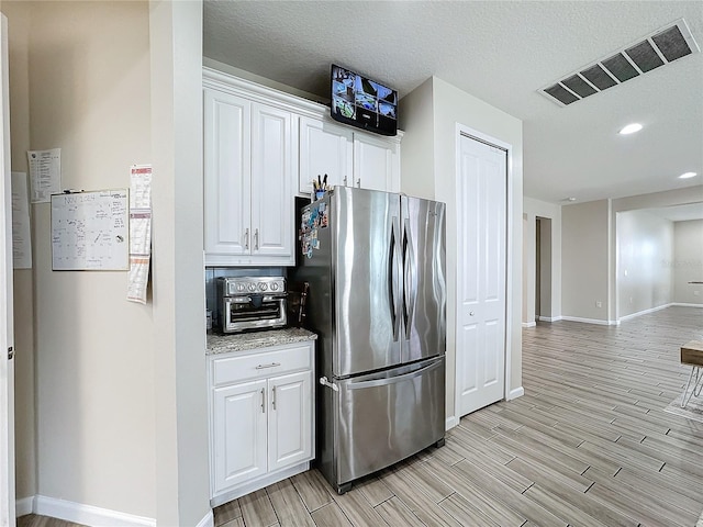 kitchen featuring white cabinets, a textured ceiling, light hardwood / wood-style floors, and stainless steel refrigerator