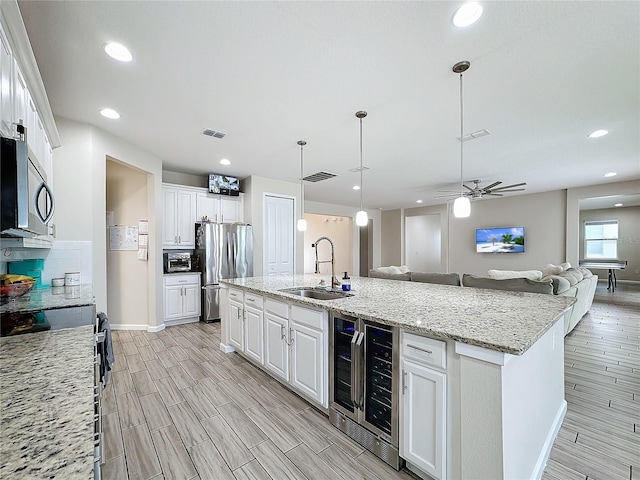 kitchen featuring white cabinetry, sink, wine cooler, a kitchen island with sink, and appliances with stainless steel finishes