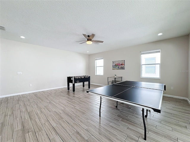 rec room featuring a textured ceiling, light hardwood / wood-style floors, plenty of natural light, and ceiling fan