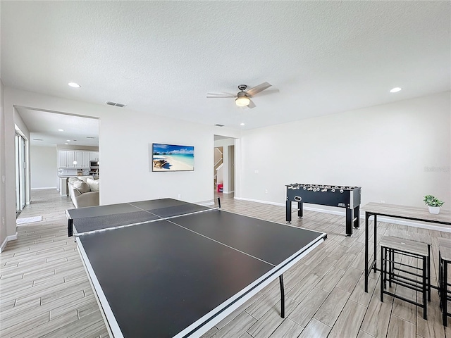 game room with a textured ceiling, light wood-type flooring, and ceiling fan