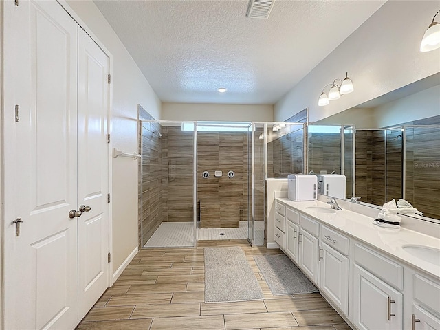 bathroom with vanity, a shower with shower door, and a textured ceiling