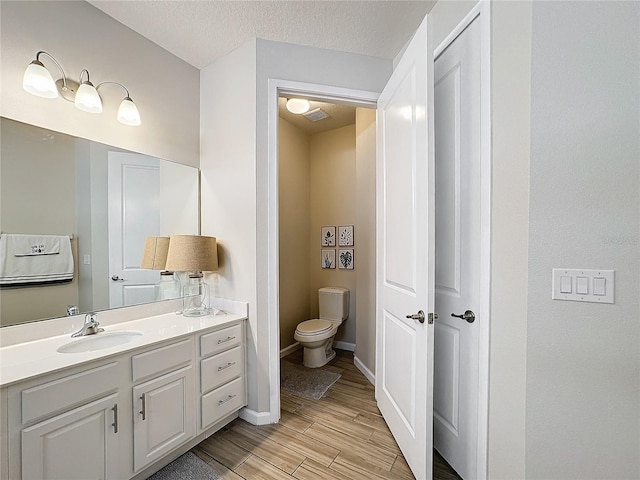 bathroom featuring hardwood / wood-style floors, vanity, toilet, and a textured ceiling