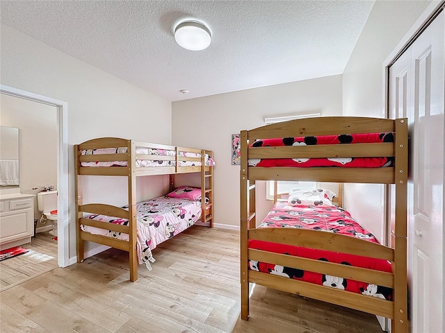 bedroom featuring ensuite bath, light hardwood / wood-style flooring, and a textured ceiling