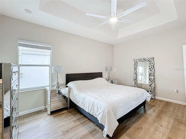 bedroom with hardwood / wood-style flooring, a raised ceiling, and ceiling fan