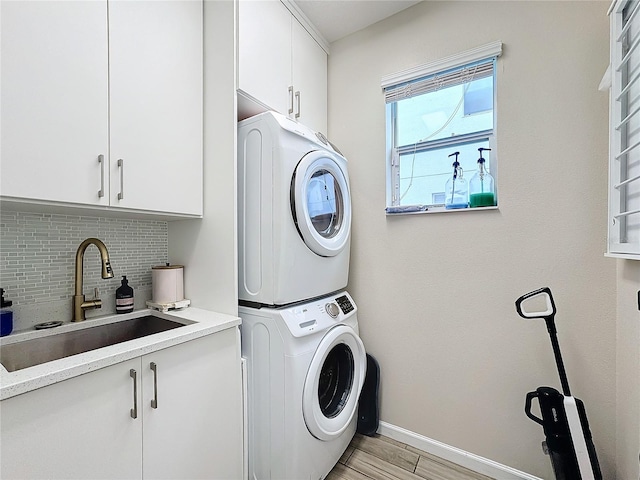 washroom featuring light hardwood / wood-style floors, cabinets, stacked washing maching and dryer, and sink