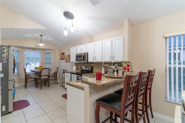 kitchen with dark stone counters, white cabinets, vaulted ceiling, kitchen peninsula, and stainless steel appliances