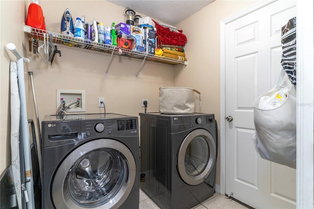 laundry area featuring washing machine and clothes dryer, light tile patterned floors, and a textured ceiling