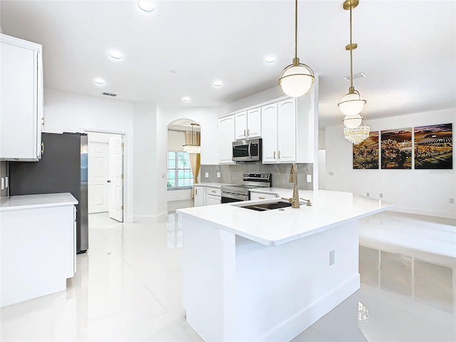 kitchen with appliances with stainless steel finishes, backsplash, sink, white cabinetry, and hanging light fixtures