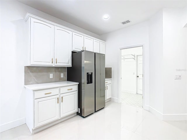 kitchen featuring decorative backsplash, stainless steel fridge, and white cabinetry