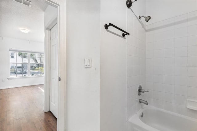 bathroom with hardwood / wood-style flooring, a textured ceiling, and tiled shower / bath