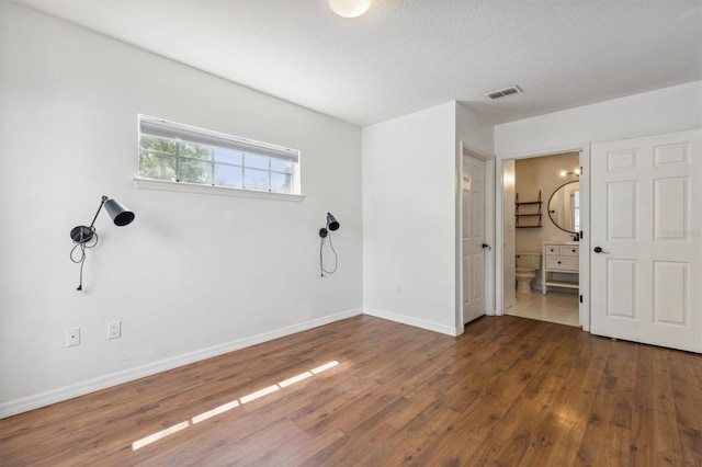 unfurnished bedroom featuring dark hardwood / wood-style floors, a textured ceiling, and ensuite bath