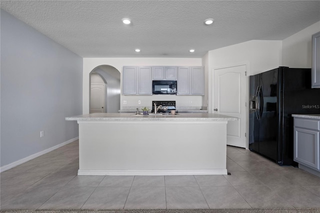 kitchen featuring a textured ceiling, sink, an island with sink, and black appliances