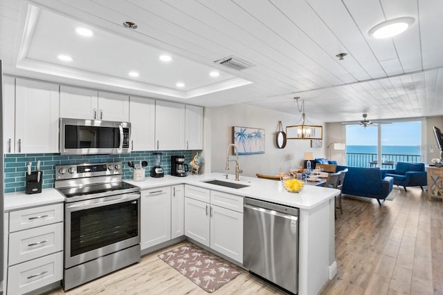 kitchen with stainless steel appliances, a water view, white cabinets, sink, and light wood-type flooring