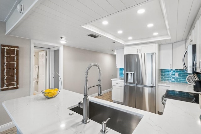 kitchen with light hardwood / wood-style floors, sink, a tray ceiling, white cabinetry, and appliances with stainless steel finishes