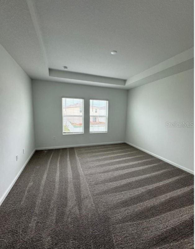 empty room featuring a textured ceiling, dark carpet, and a tray ceiling