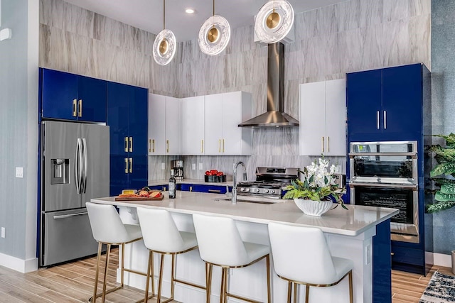 kitchen with white cabinetry, hanging light fixtures, stainless steel appliances, light hardwood / wood-style floors, and a center island with sink