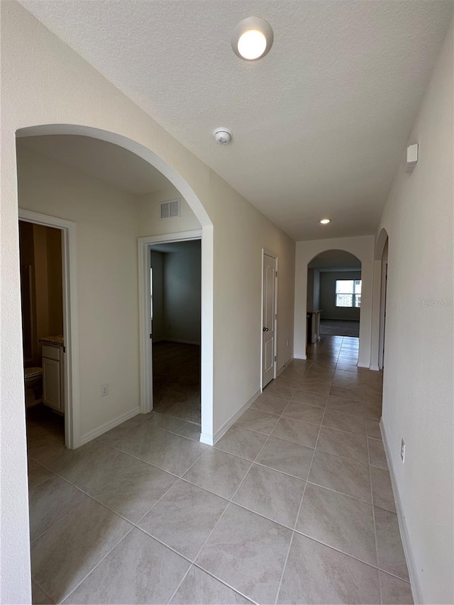 hallway with a textured ceiling and light tile patterned floors