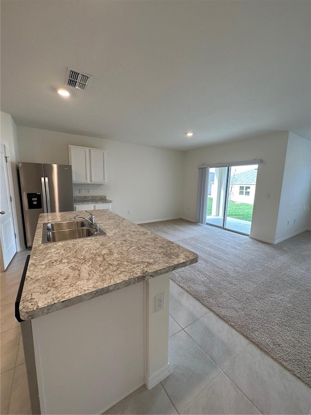 kitchen with white cabinetry, sink, stainless steel refrigerator with ice dispenser, light tile patterned floors, and a kitchen island with sink