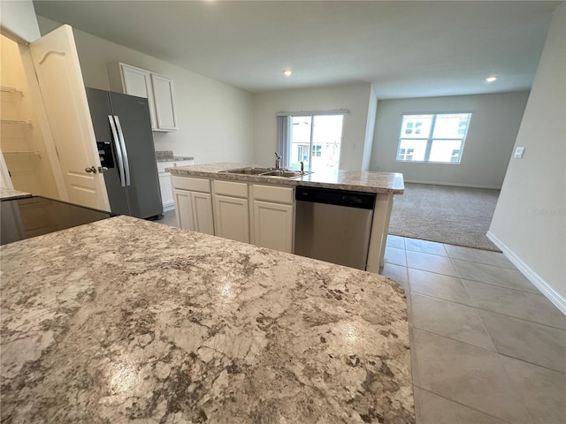 kitchen featuring stainless steel appliances, light colored carpet, white cabinets, sink, and a kitchen island with sink