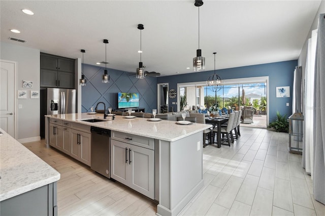 kitchen featuring a center island with sink, sink, appliances with stainless steel finishes, decorative light fixtures, and gray cabinetry