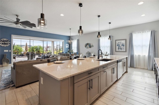 kitchen with light stone counters, a center island with sink, pendant lighting, sink, and dishwasher