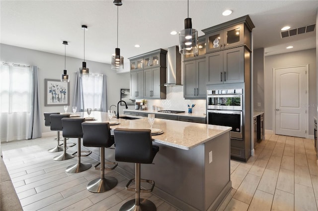 kitchen featuring wall chimney exhaust hood, a healthy amount of sunlight, light stone counters, and an island with sink