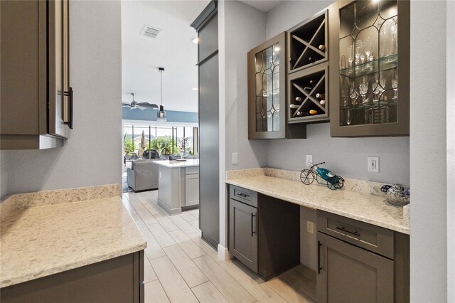 bar featuring dark brown cabinets, hanging light fixtures, and light stone counters